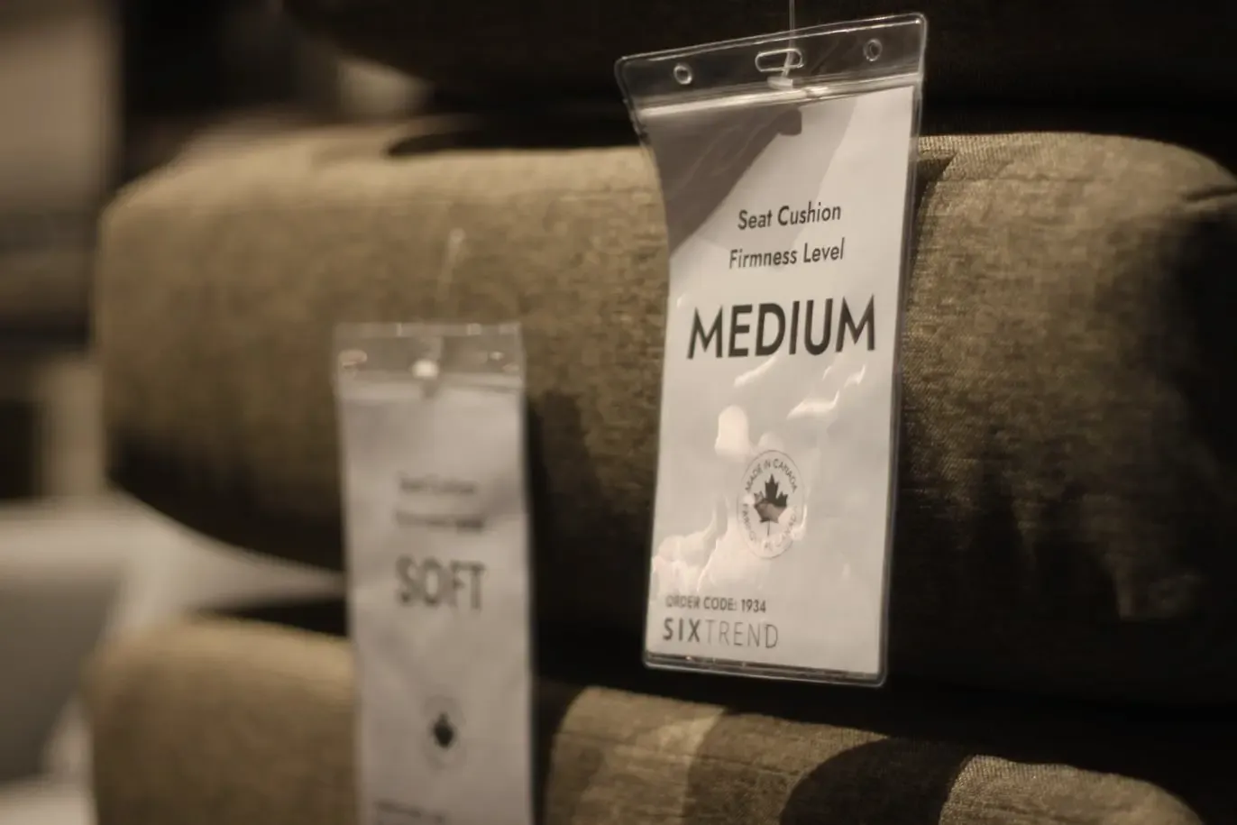 Two cushion firmness tags labelled SOFT and MEDIUM hanging on grey upholstered seat cushions with a Made in Canada seal.