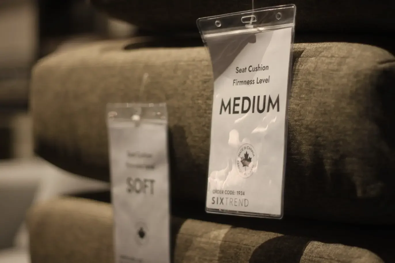 Two cushion firmness tags labelled 'SOFT' and 'MEDIUM' hanging on grey upholstered seat cushions with a Made in Canada seal.