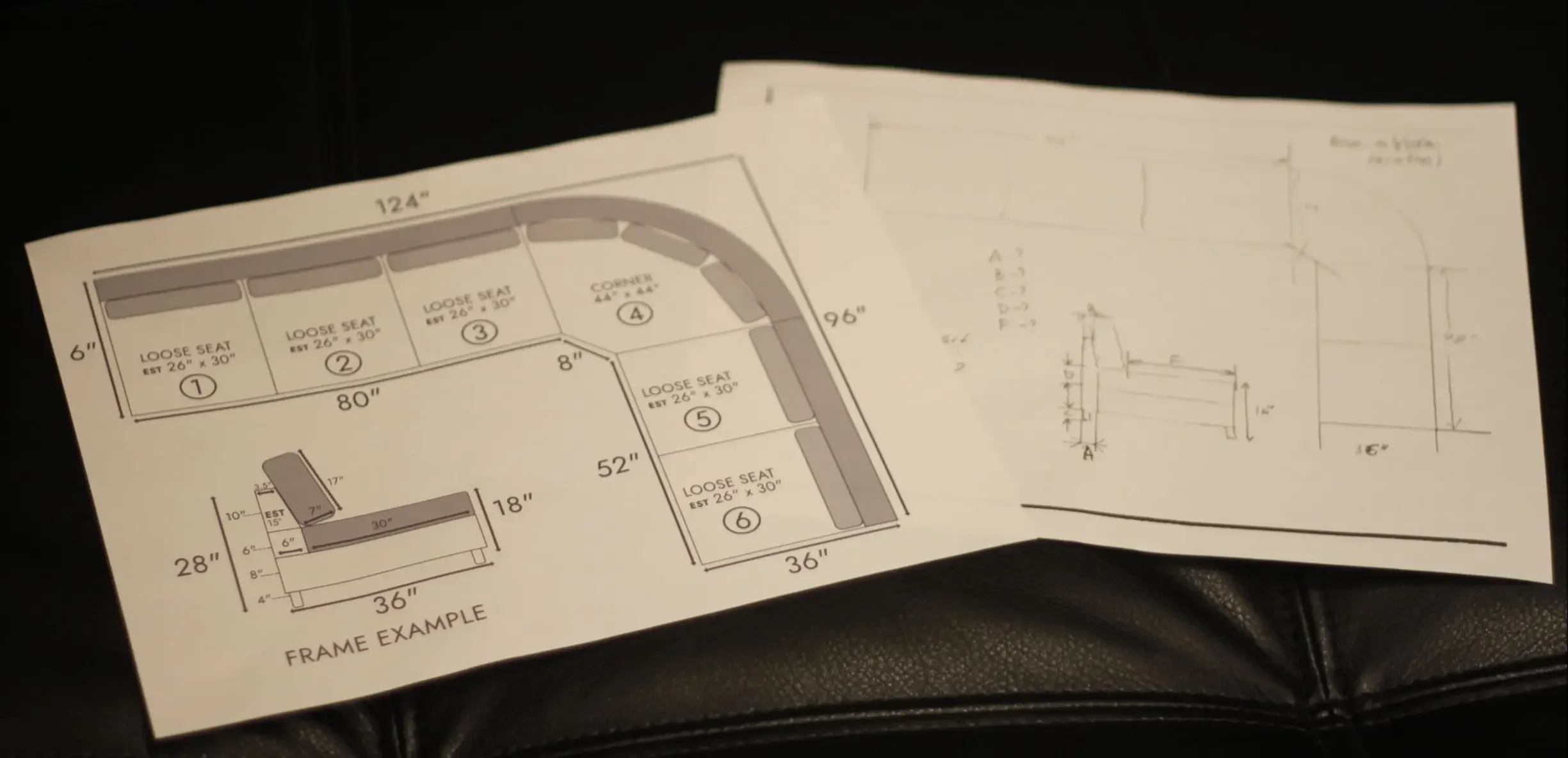 Hand-drawn sectional sofa floor plan with detailed measurements and a side-view frame example sketch resting on a black leather background.