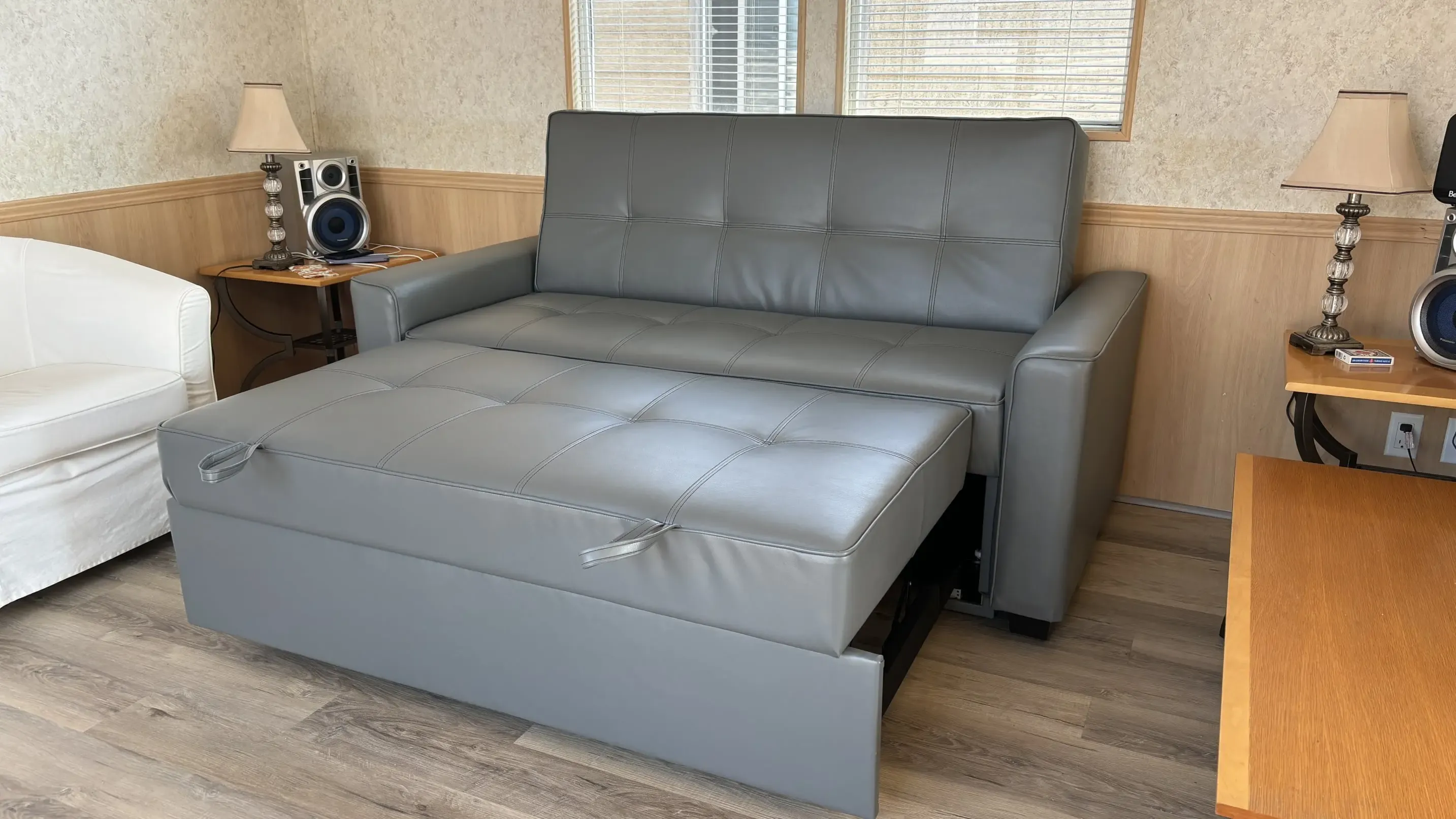 A SIXTREND Flex sofa bed with extended trundle in a customer's home, photographed against a wood-panelled wall with table lamps and a vintage stereo.