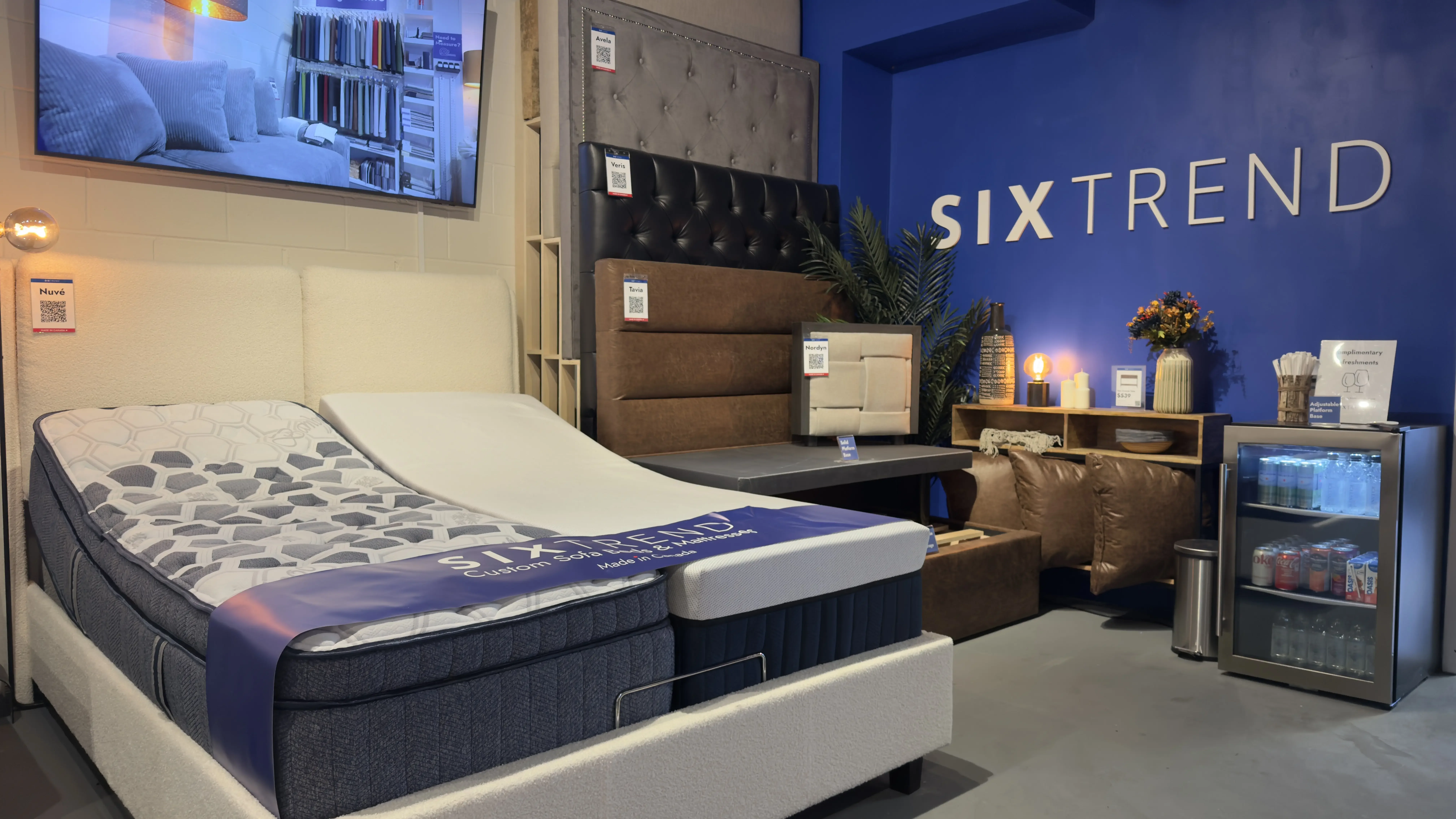 Showroom display of an adjustable bed frame with a pocket-coil hybrid mattress beside a tufted leather headboard.
