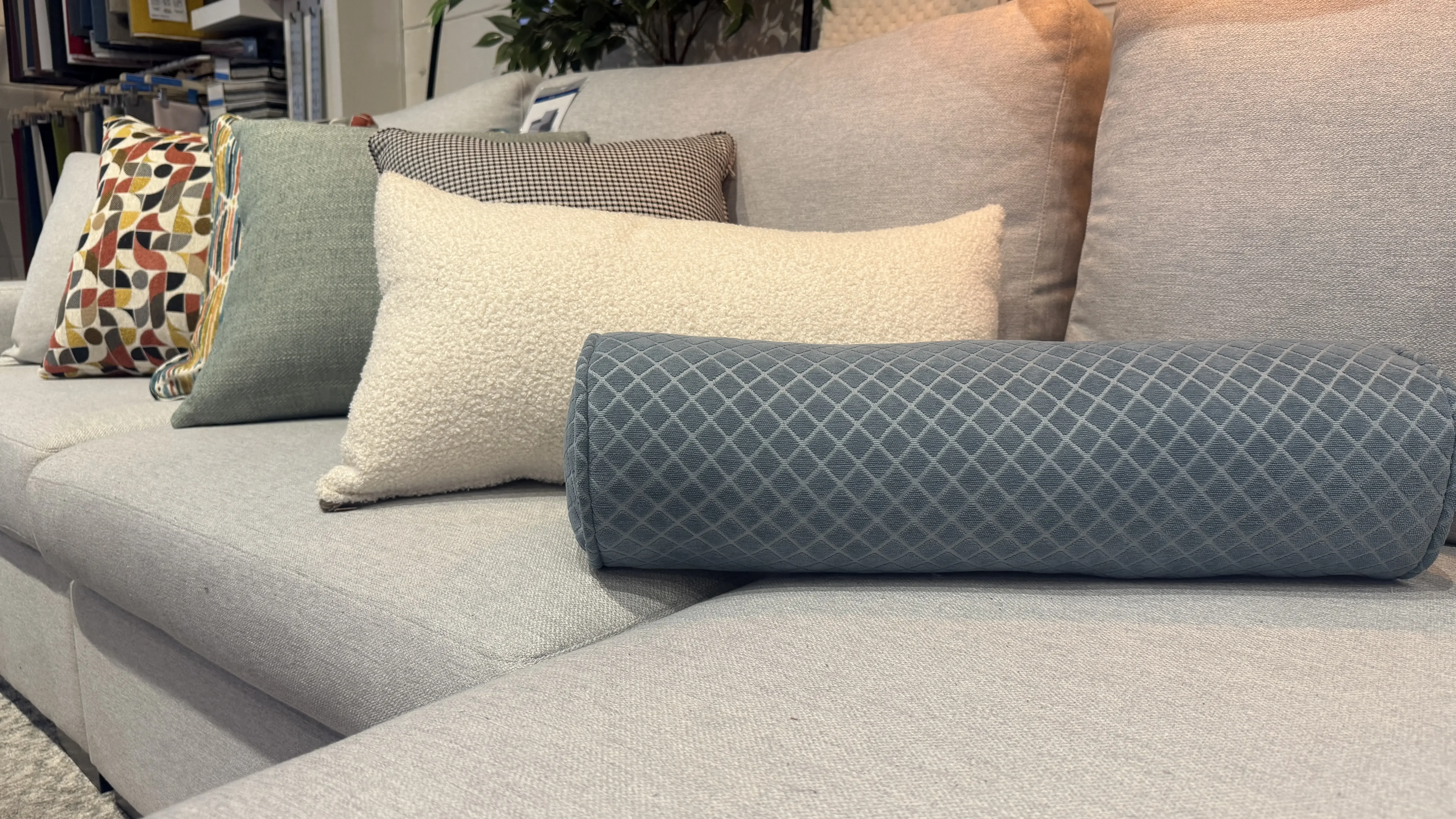 Decorative cushions and a long bolster pillow in mixed patterns and textures arranged on a grey sofa.