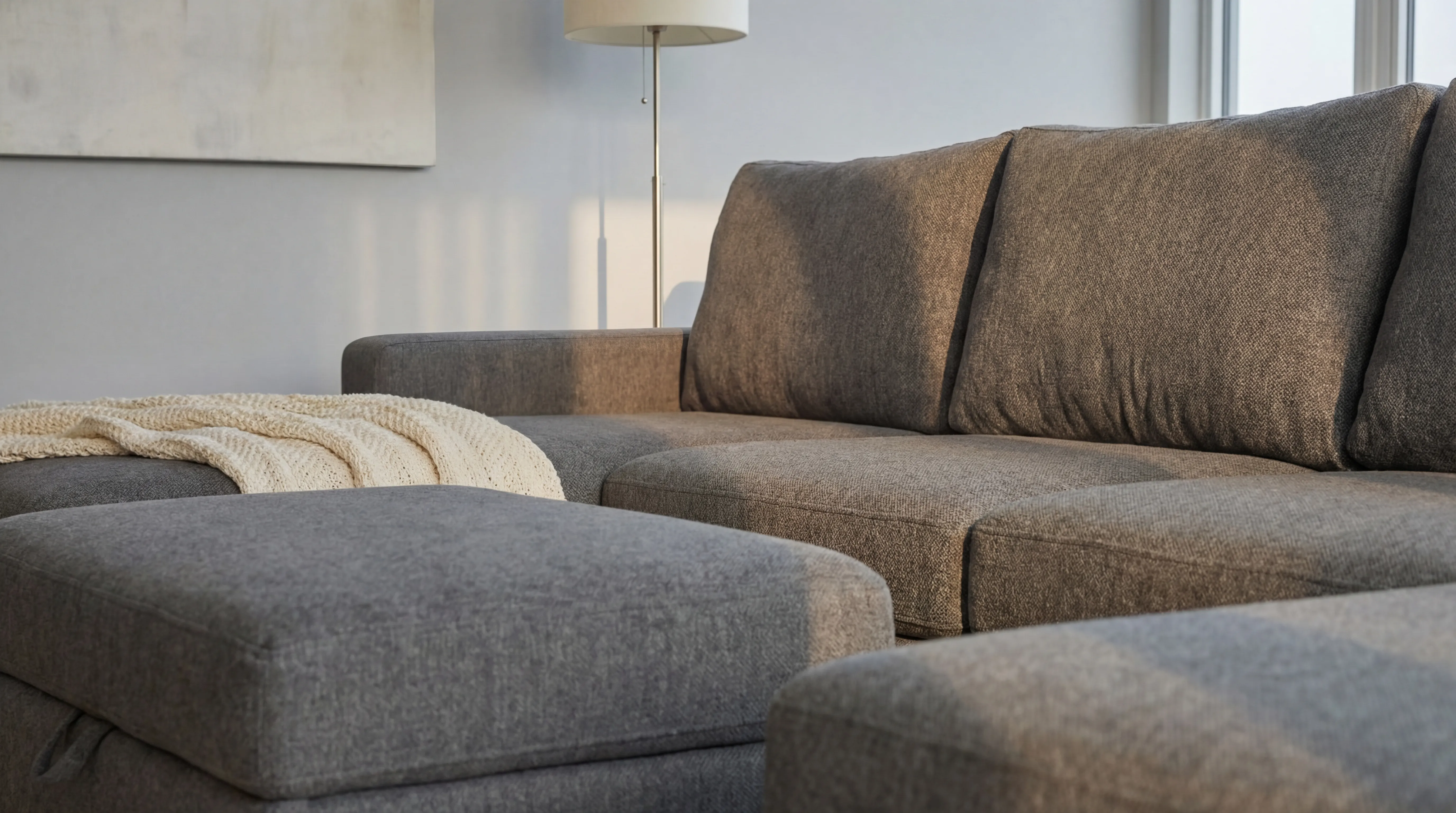 Close-up corner detail of a custom-sized charcoal-grey fabric sectional with chaise and cream throw blanket